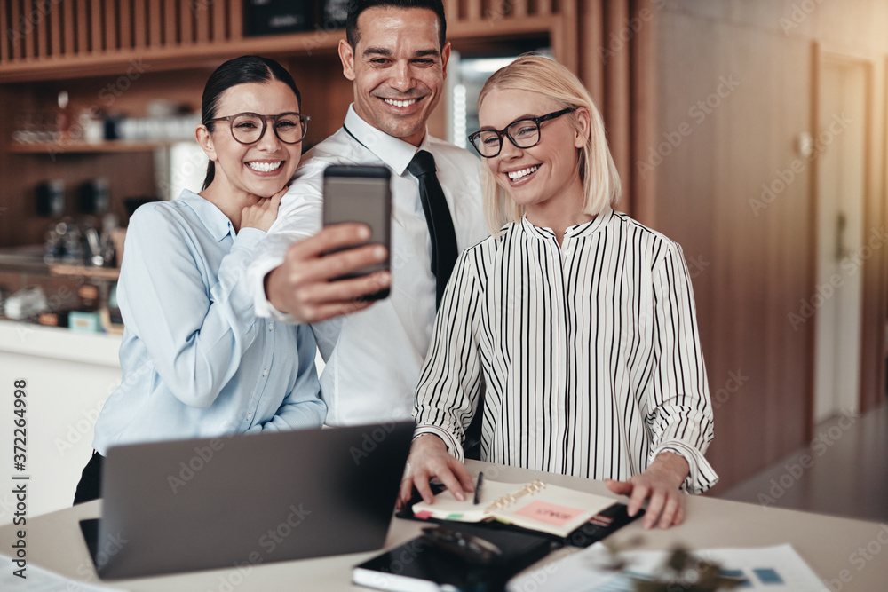Smiling young businesspeople taking selfies together at work Smiling young businesspeople taking selfies together at work