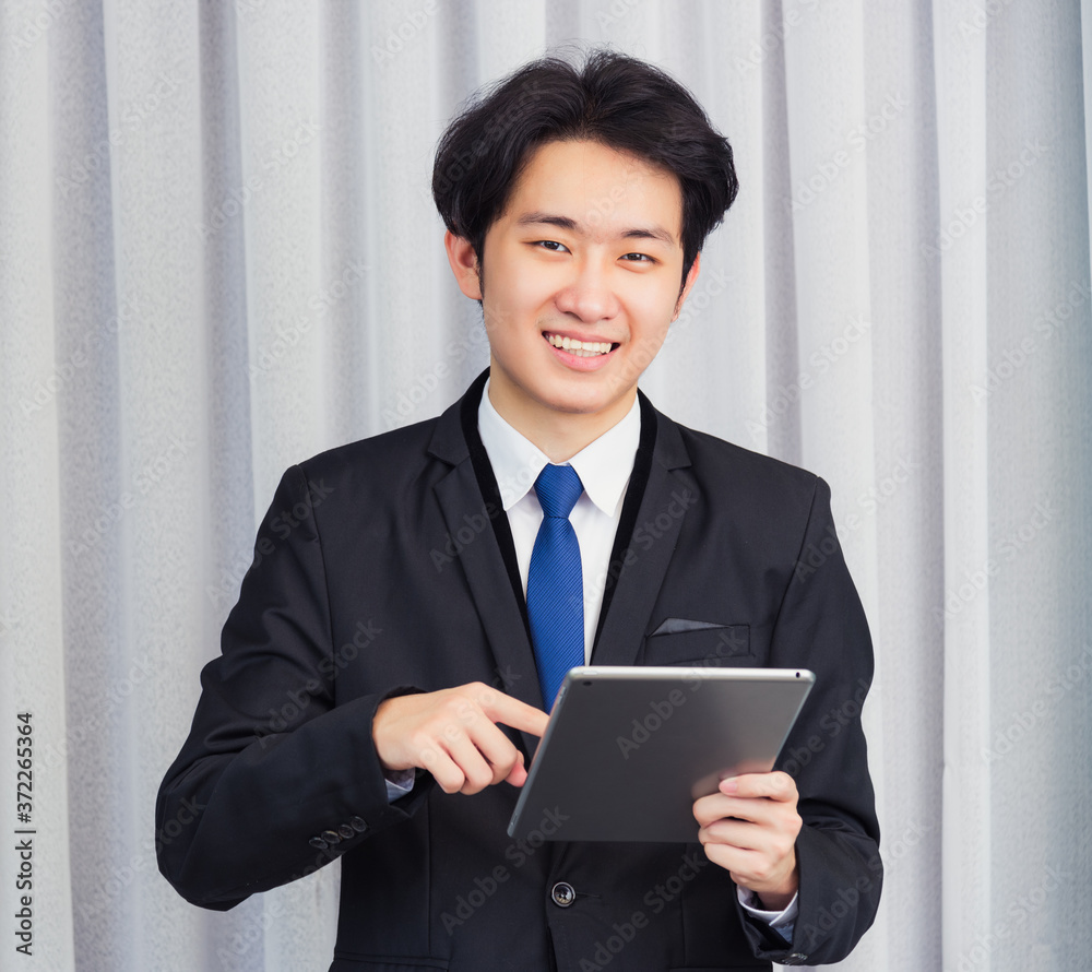 Work from home, Asian young businessman wear suit video conference call or facetime he smiling using smart digital tablet computer and point finger on the screen at home office, looking to camera Work from home, Asian young businessman wear suit video conference call or facetime he smiling using smart digital tablet computer and point finger on the screen at home office, looking to camera