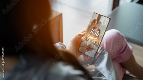 Back view of woman browsing work opportunities online using job search smartphone app after being laid off during covid-19 or coronavirus outbreak at home.find your career and recruitment concept.