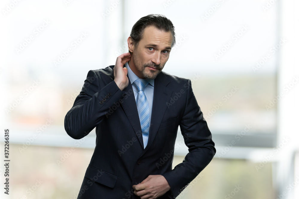 Handsome mature businessman preens before camera. Attractive caucasian businessman is preening against blurred background. Handsome mature businessman preens before camera. Attractive caucasian businessman is preening against blurred background.