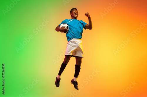 High jumping winner. Male soccer, football player training in action isolated on gradient studio background in neon light. Concept of motion, action, ahievements, healthy lifestyle. Youth culture. © master1305