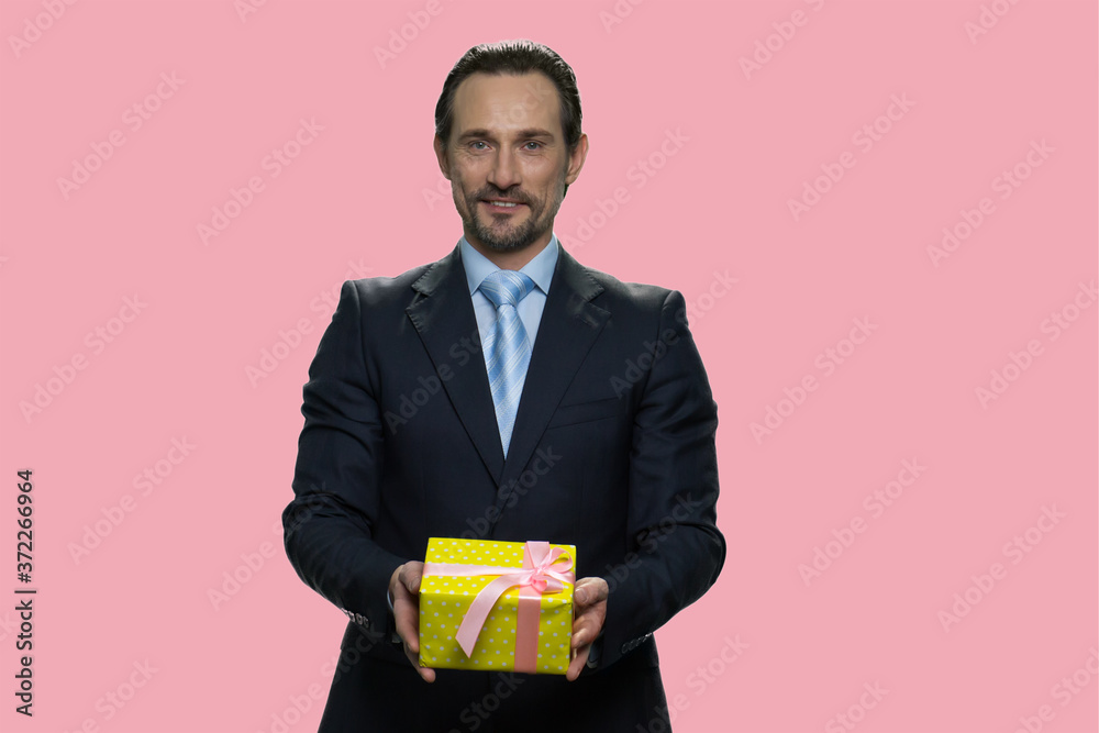 Portrait of businessman giving gift box. Handsome mature man in suit offering present box on color background. Beautiful gift for her. Portrait of businessman giving gift box. Handsome mature man in suit offering present box on color background. Beautiful gift for her.