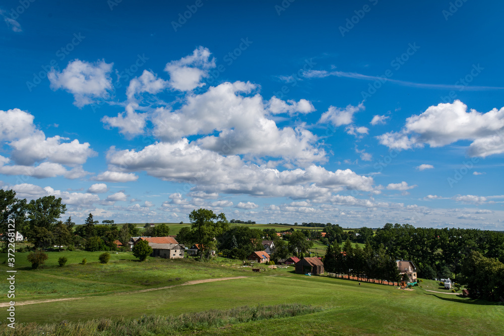 View from the top of a hill showing vast areas of meadows, forests, orchards, fields, and pasturelands connected together below a cloudy summer sky seen on a Polish countryside during a hike View from the top of a hill showing vast areas of meadows, forests, orchards, fields, and pasturelands connected together below a cloudy summer sky seen on a Polish countryside during a hike