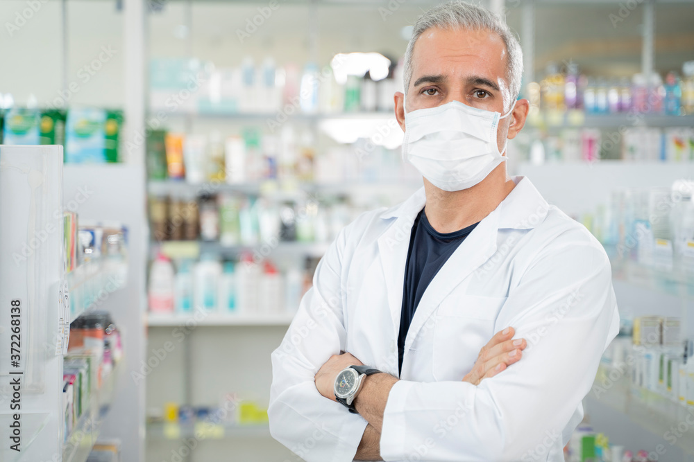 Young male pharmacist standing with arms crossed.
