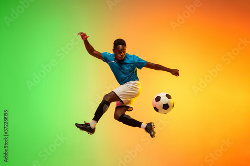 High jumping. Male soccer, football player training in action isolated on gradient studio background in neon light. Concept of motion, action, ahievements, healthy lifestyle. Youth culture. © master1305