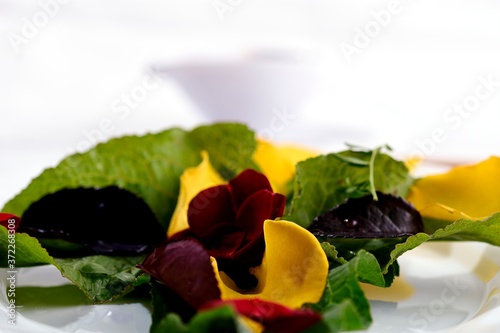 Salad with rose petals, including rose leaves, lentils and beans, and wild leaves. In the background a dressing in a bowl