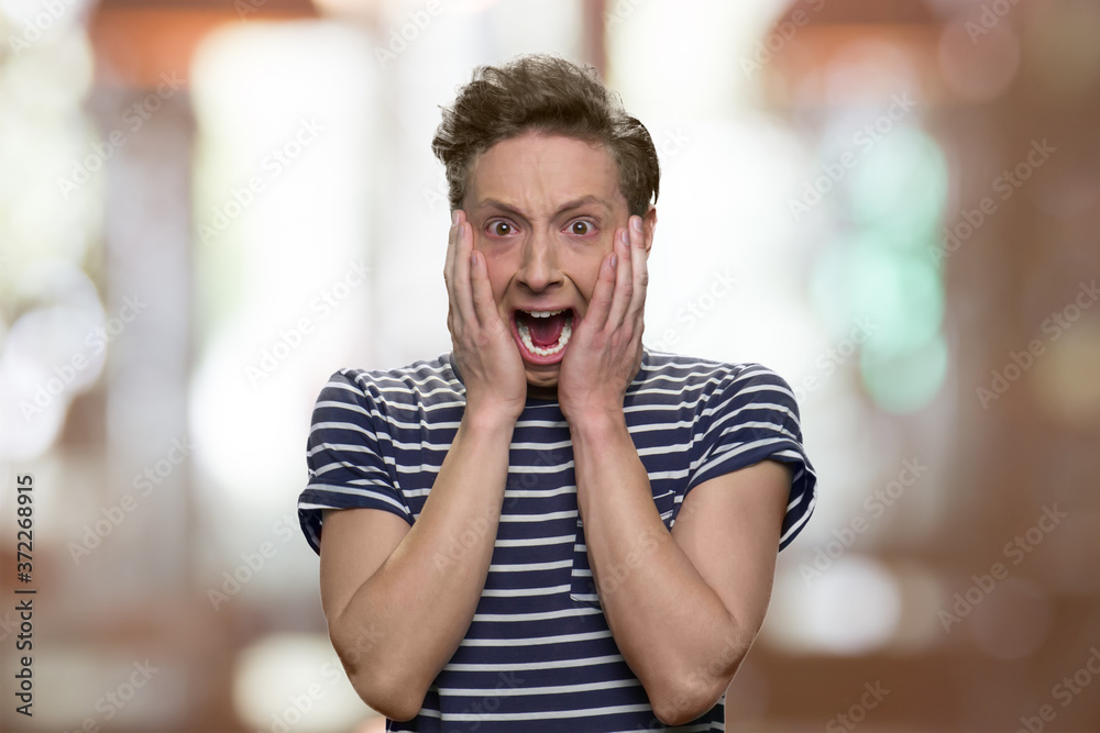 Scared teen boy is screaming on abstract blurred background. Frightened  teenage guy holding hands on face. Stock Photo | Adobe Stock