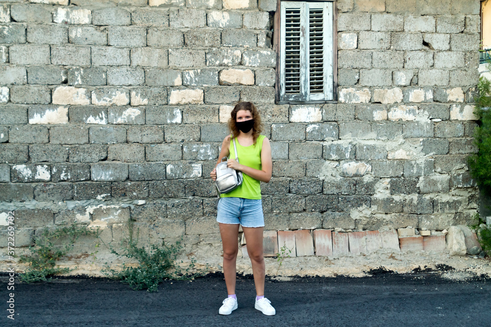 Girl in protective face mask standing in front of old stone house wall