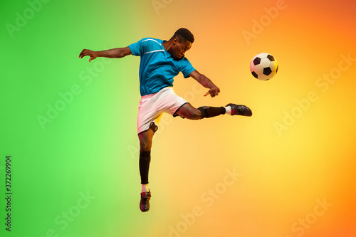 High jumping. Male soccer, football player training in action isolated on gradient studio background in neon light. Concept of motion, action, ahievements, healthy lifestyle. Youth culture. © master1305
