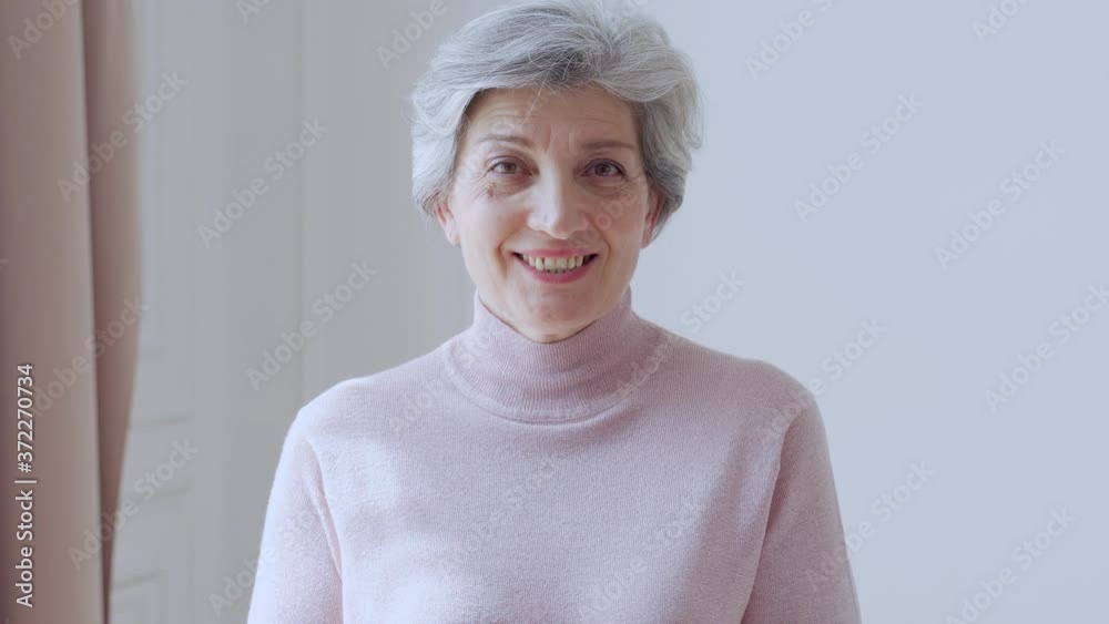 Beautiful old woman with gray hair smiles standing at home