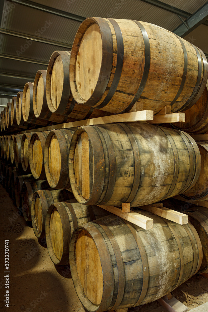 A row of stacks of traditional full whisky barrels, set down to mature, in a large warehouse