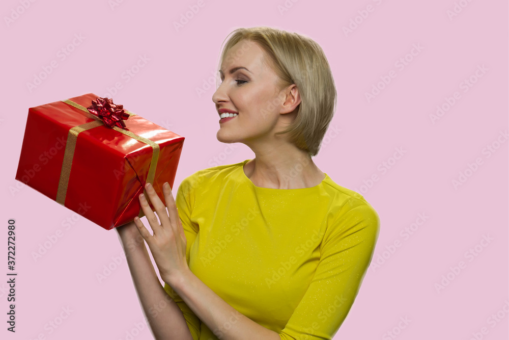 Happy woman looking at gift box in her hands. Pretty smiling girl holding present box on color background. Gift for special occasion. Happy woman looking at gift box in her hands. Pretty smiling girl holding present box on color background. Gift for special occasion.