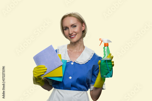 Housekeeper in uniform holding cleaning supplies. Portrait of beautiful smiling chambermaid with rags and detergents. House cleaning service concept.