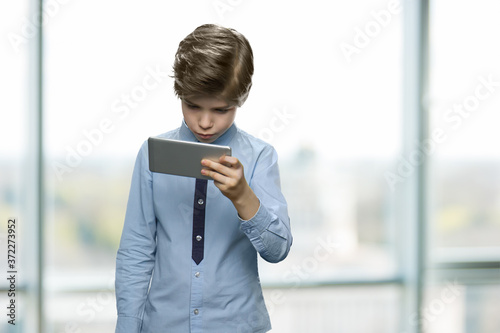 Handsome caucasian boy using smartphone. Little boy looking at mobile phone standing on blurred background. Children, technology, internet addiction and people concept.