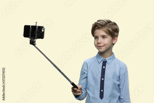 Cute little boy using selfie stick. Handsome caucasian child taking picture with monopod isolated on white background. Children and modern technology concept.