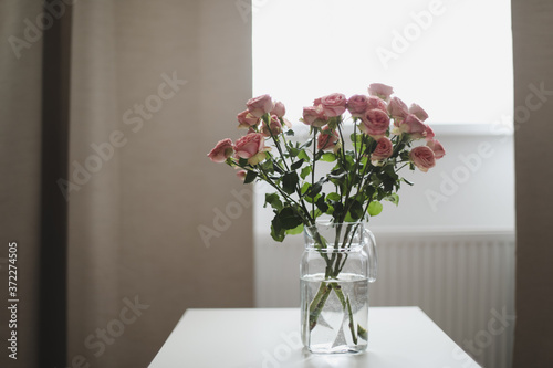Pink roses flowers bouquet in glass vase against the window. Holiday celebration concept. Interior decoration