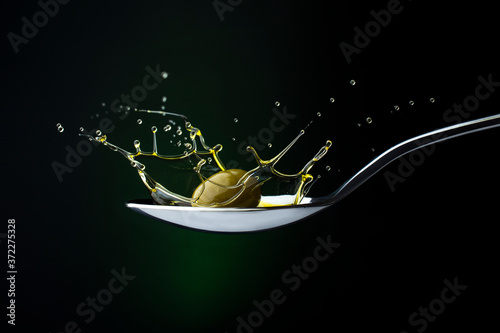 closeup of green olive with splashing oil on a spoon on a dark background