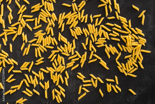 top view of raw penne pasta scattered on black background