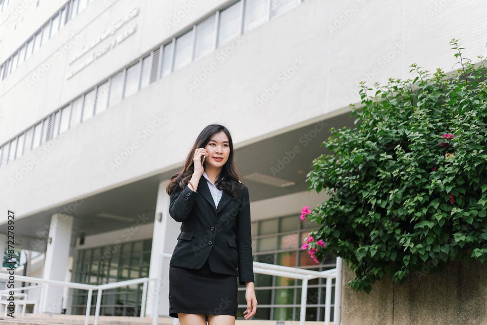 Fototapeta premium Beautiful asian business woman talking on cellphone while walking outdoor