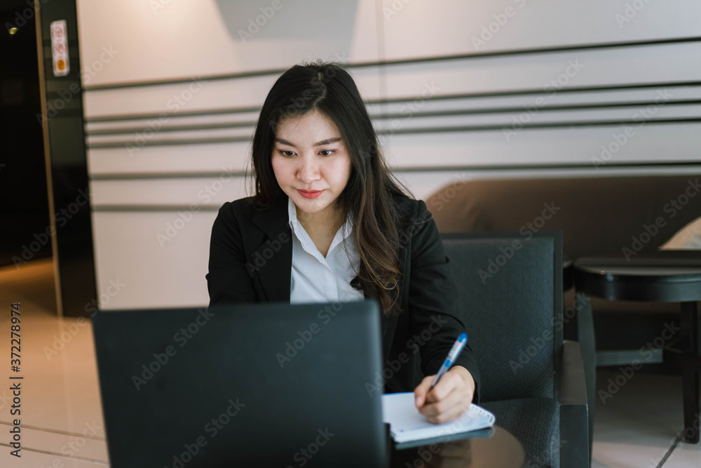 Beautiful young asian woman in suit using laptop and writing note Beautiful young asian woman in suit using laptop and writing note