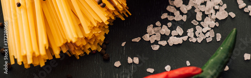 close up view of raw Italian spaghetti with salt on black background, panoramic shot photo