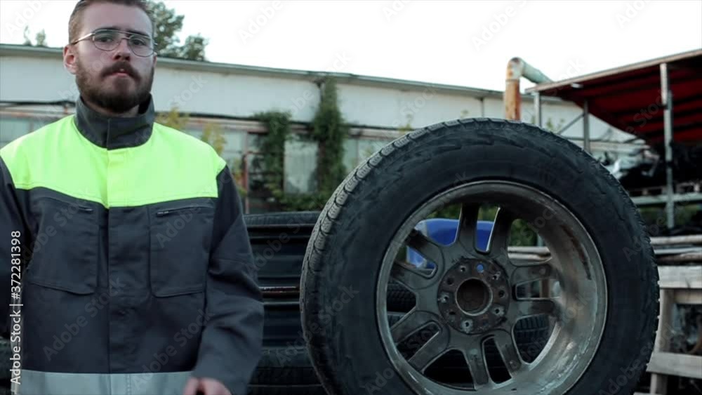 A handsome young auto mechanic walks through the rows of tires and stops at a large wheel arms crossed over chest. Close-up. Slow motion A handsome young auto mechanic walks through the rows of tires and stops at a large wheel arms crossed over chest. Close-up. Slow motion