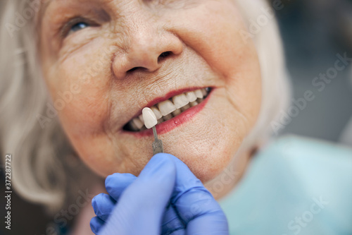 Elderly woman choosing color of teeth while sitting in the dentist chair