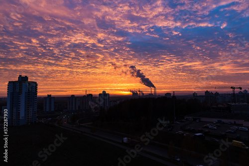 A bright colorful sunset over a thermal power plant in a quiet sleeping area West in Minsk, Belarus. Issues and problems of ecology within the city and beyond. The smoke is illuminated by the sun. 