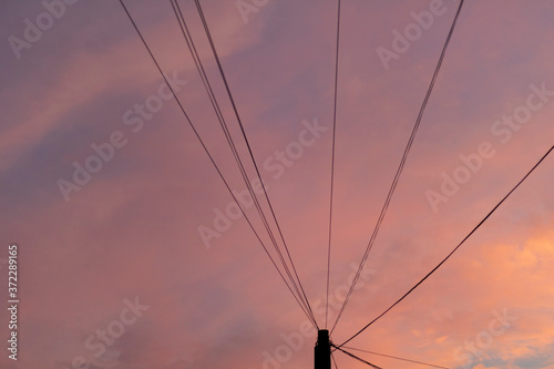 Electric pole with wires on a bright, colorful sky during sunset.