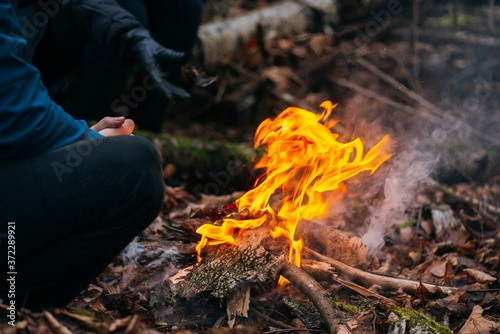 Man warms his hands on fire. Burning wood at evening in the forest. Campfire at touristic camp at nature. Barbeque and cooking outdoor fresh air. Flame and fire sparks on dark abstract background