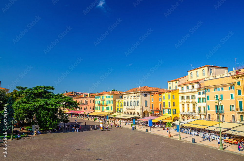 Piazza Bra square aerial view in Verona city historical centre with row of old colorful multicolored buildings cafes and restaurants, green trees and walking tourists, Veneto Region, Northern Italy