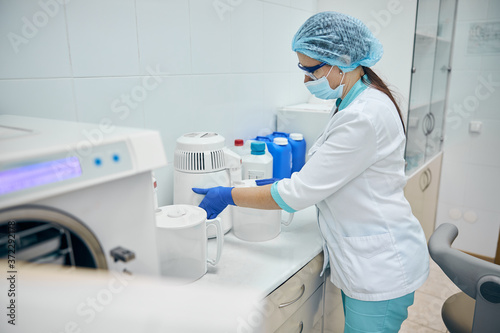 Woman wearing protective uniform and glasses taking care of the modern machine