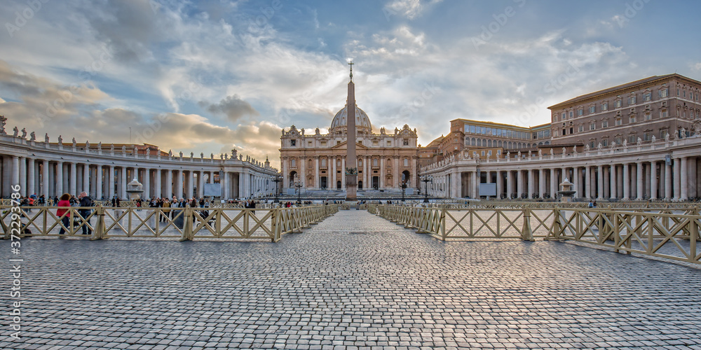 Tourists visit the St. Peter's Basilica in Vatican City. Panorama view of Saint Peter's Basilica and the Egyptian obelisk at the center of the Vatican square on sunrise in Vatican, Rome, Italy