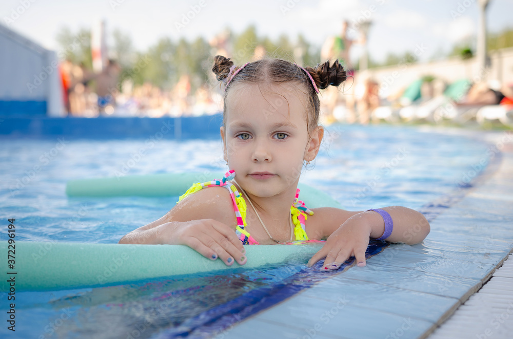 little beautiful girl swimming with a foam noodle in a outdoor pool. summer vacation in the water park
