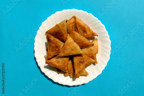 Famous traditional Arabic, Middle East, Asian cuisine. Triangular arabic chicken samosa on bright blue background. Many mini samosas on white plate photo