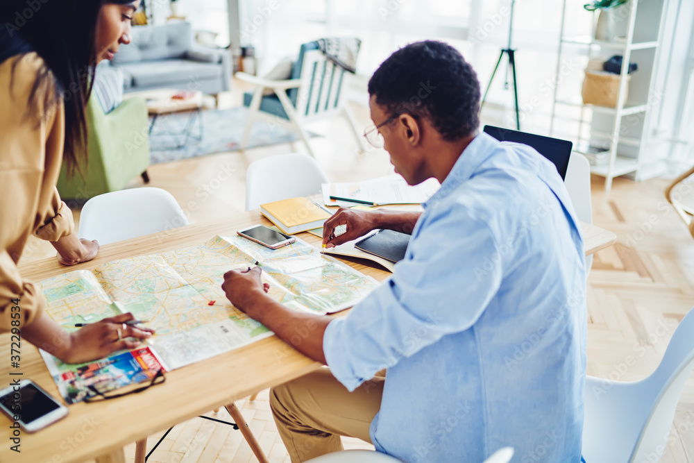African american hipster guy pointing on map share ideas for travel adventure with female friend sitting at desktop at home interior, dark skinned young woman and man discussing route for journey.