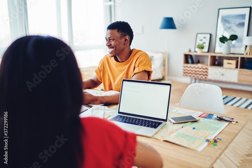Cropped image with back view of woman sitting at table near cheerful african american male student, smiling dark skinned hipster guy satisfied with communication during planning trip using netbook.