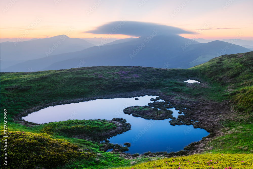 Mountain lake on sunrise time. Picturesque summer landscape with green mountain hills and sun rays in morning sky. Carpathian mountains