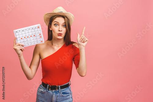 Portrait of a funny young girl holding periods calendar isolated over pink background.