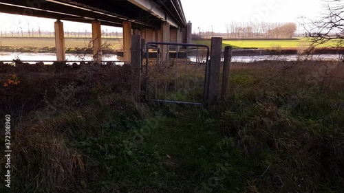 Elsloo en Meers, South Limburg / Netherlands, December 19th, 2019. Metal gate with a barbed wire fence, with the Maas river in the background under the Scharbergbrug or Maas bridge on the A76 road photo