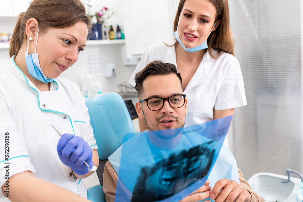 Fototapeta premium Female dentist with an assistant showing dental x-ray of teeth to a male patient in the clinic.