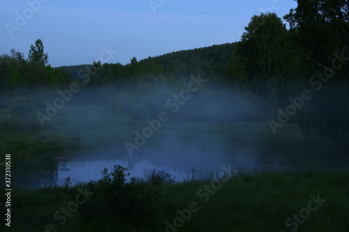 Thick white fog over a forest lake at dusk. Warm summer in the foothills of the Western Urals.