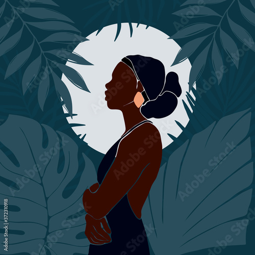 Young African American woman stands in profile against the background of the moon. Night in the jungle. Large tropical leaves. Dark blue vector illustration in flat style.
