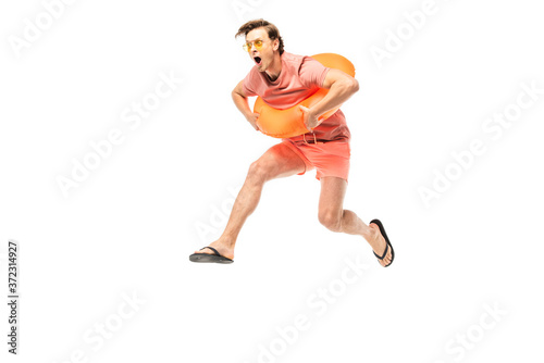 Excited man in sunglasses, flip flops and swim ring jumping isolated on white