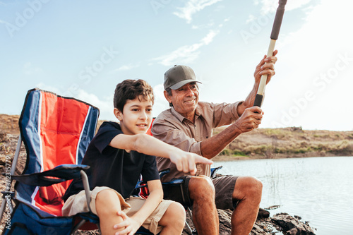Latin grandfather and grandson enjoying day together fishing on the lake. The boy points towards the water. © kleberpicui