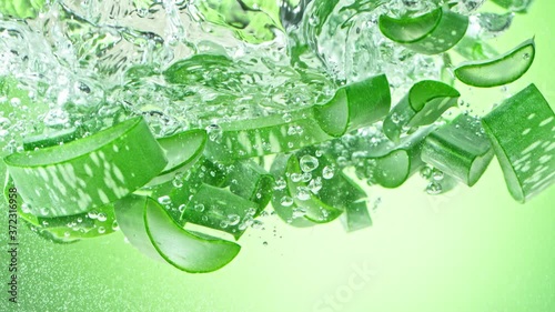 Super Slow Motion Shot of Aloe Vera Cuts Falling into Water on Green Background at 1000fps.