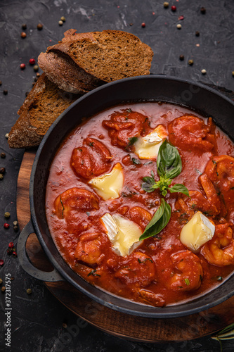 Shrimp and seafood in tomato sauce with herbs on a dark concrete table