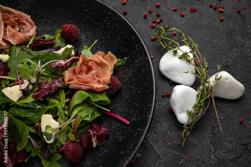Salad with ham, herbs, raspberries, microgreens on a dark concrete table