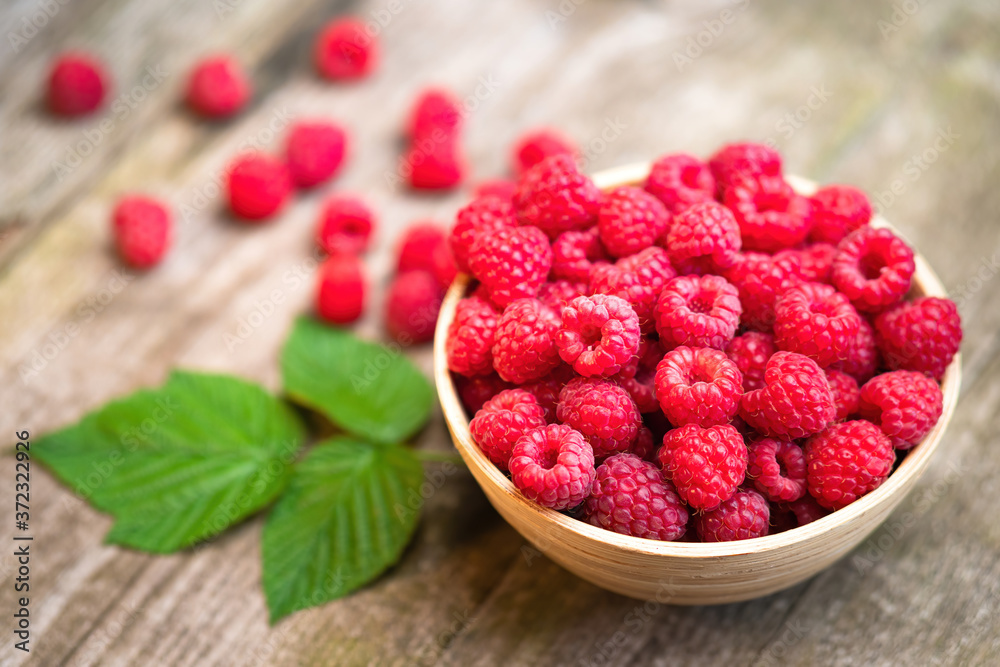 Fresh ripe red raspberries with leaves in a bowl on rustic old wooden table. Healthy organic food, summer vitamins, BIO viands, natural background. Copy space for your advertising text message Fresh ripe red raspberries with leaves in a bowl on rustic old wooden table. Healthy organic food, summer vitamins, BIO viands, natural background. Copy space for your advertising text message