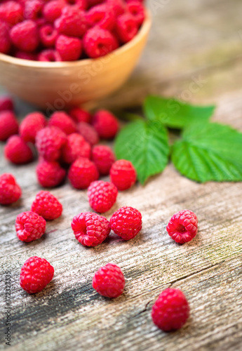 Fresh ripe red raspberries with leaves in a bowl on rustic old wooden table. Healthy organic food, summer vitamins, BIO viands, natural background. Copy space for your advertising text message